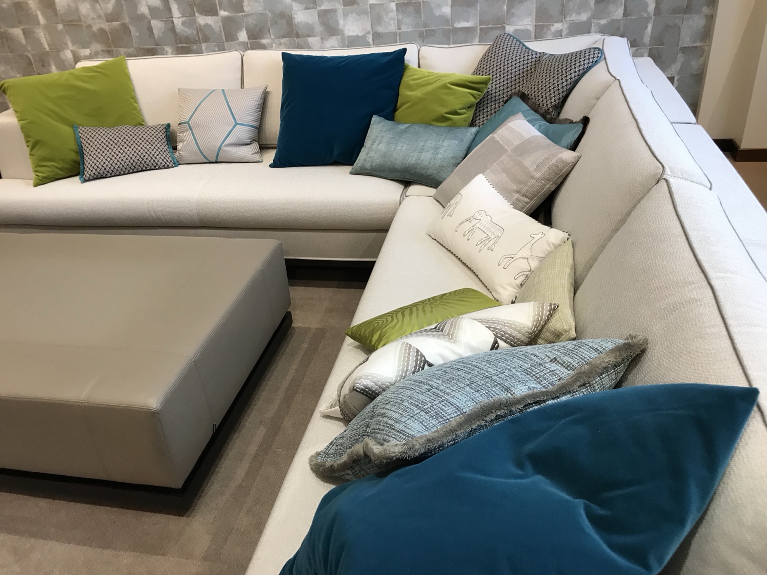 Zierkissen in Blau, Türkis, Grün und gemusterten Stoffen auf einem hellen Ecksofa