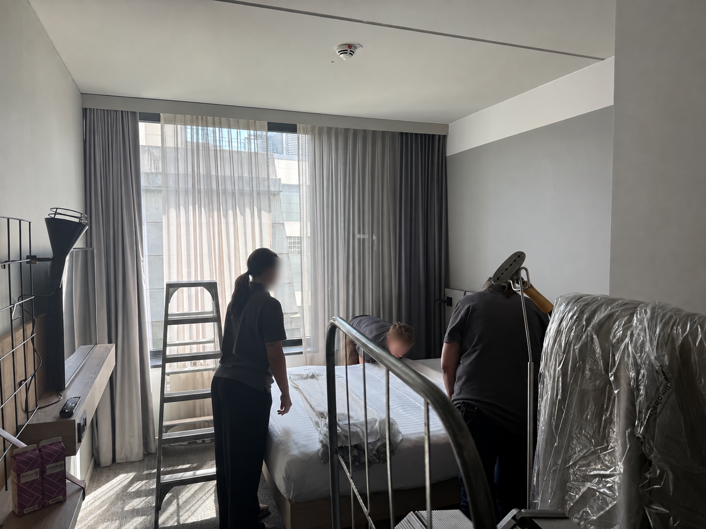 Montage der Stores und Verdunkelungsvorhänge im Hotelzimmer; Gesichter der Mitarbeitenden unscharf