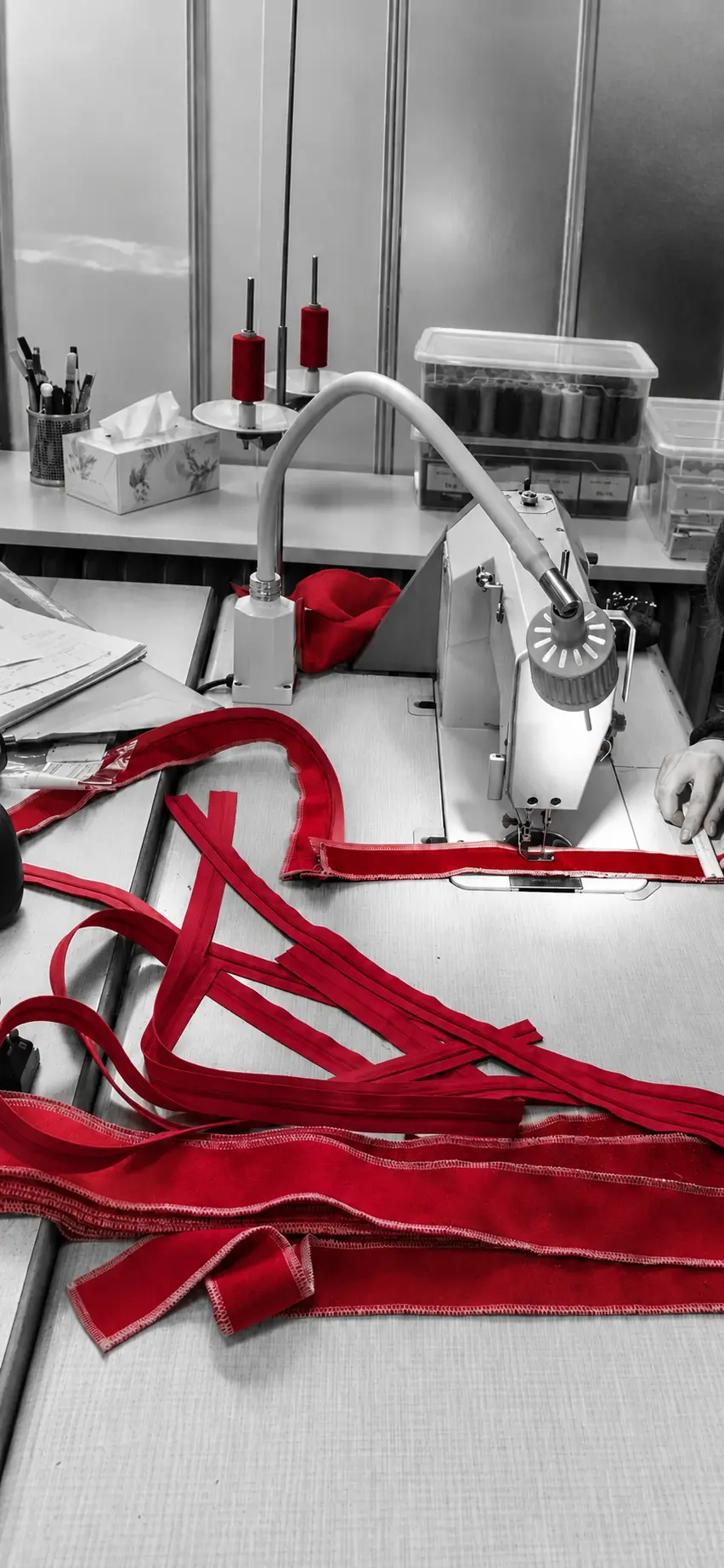 Rote Stoffkeder und Reißverschlüsse werden an der Nähmaschine gefertigt.